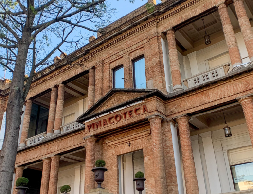 Foto da fachada da Pinacoteca durante o dia. Amplas pilastras e paredes em tijolos sem revestimento.